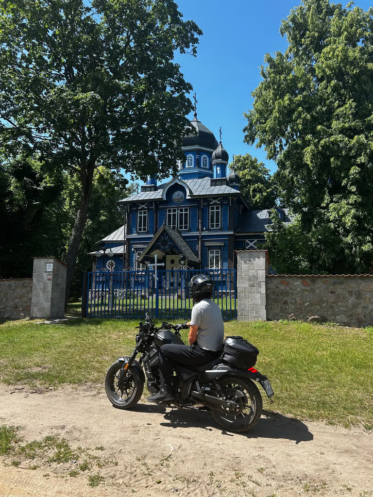 Motocyklista przed drewnianą cerkwią na Podlasiu